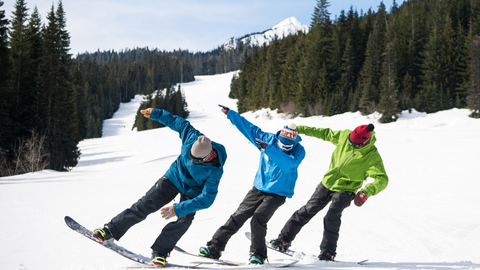 Three snowboarders stand on their edge having fun.