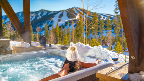 a woman wearing a white beanie hat sits in a hot tub in lodging at Winter Park Resort