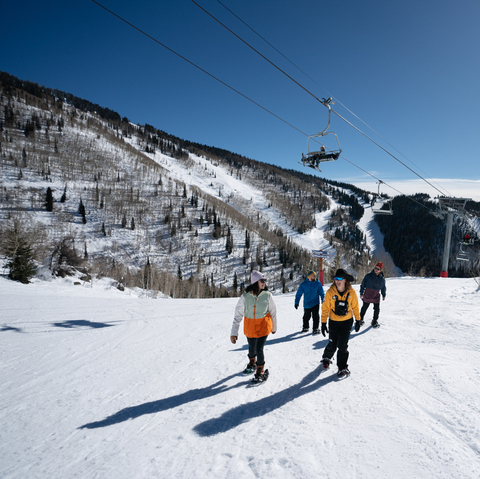 A group of people walking on a snowy slope with a ski lift in the background.