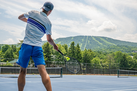 Adult serving a tennis ball on and outdoor tennis court at stratton mountain