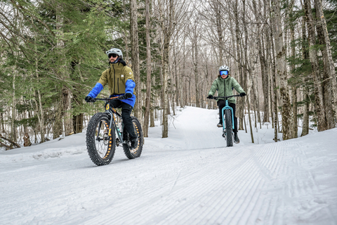 Two people riding fat bikes through the woods on groomed Nordic trails in winter 