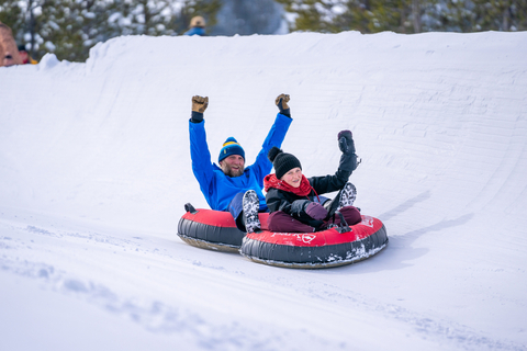 a father and son slides down the Coca Cola Tubing Hill with their hands in the air while on red snow tubes at Winter Park Resort