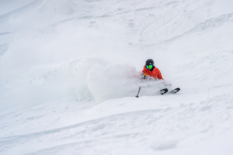 Skier in an orange jacket shreds powder and creates a snow cloud