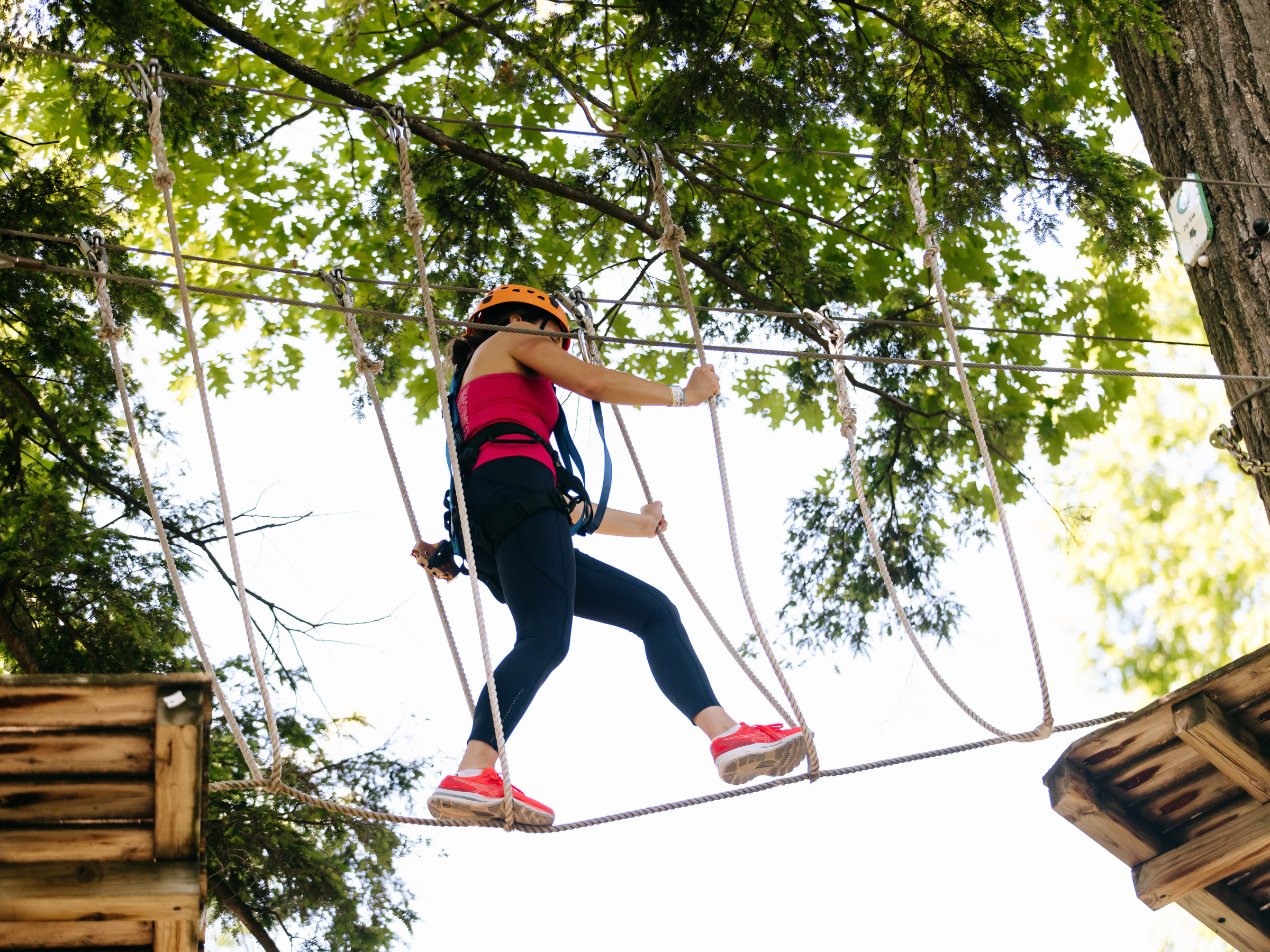 a climber steps across a suspended rope bridge element on the outdoor high ropes course challenge