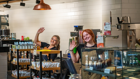 Two Brew 62 employees wave at the camera from behind the counter. 