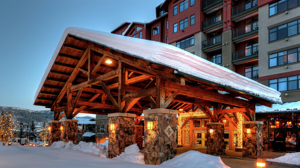 A snow-covered wooden structure with stone pillars and lights at the entrance of a building.