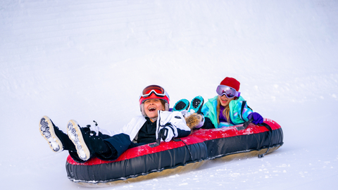 two smiling girls slide down the Coca Cola Tubing Hill on red snow tubes at Winter Park Resort